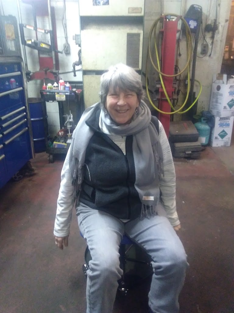 Person seated inside an auto repair bay with tools and equipment behind them